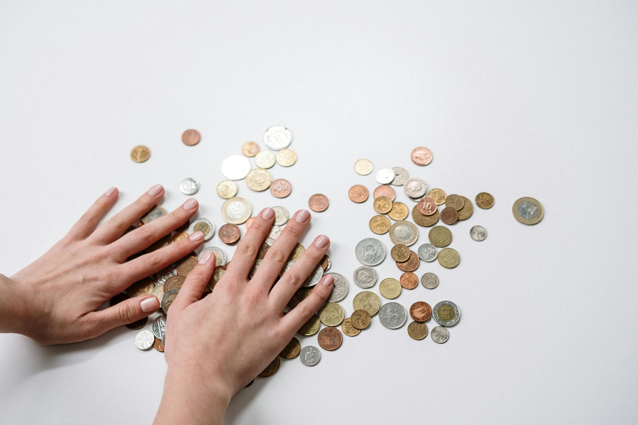 hands arranging a variety of international coins on a neutral light background. 3943720 scaled 1