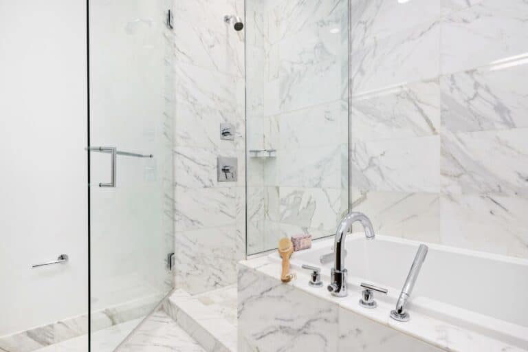 A bathroom with white marble walls and a glass shower.